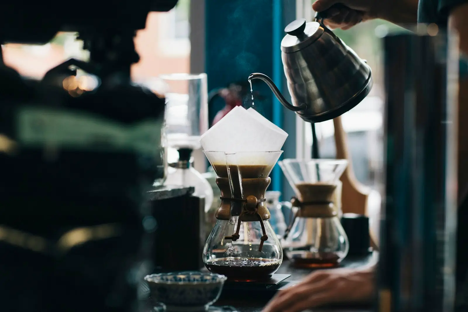 barista pouring hot water into a pour-over coffee brewer at a café bar